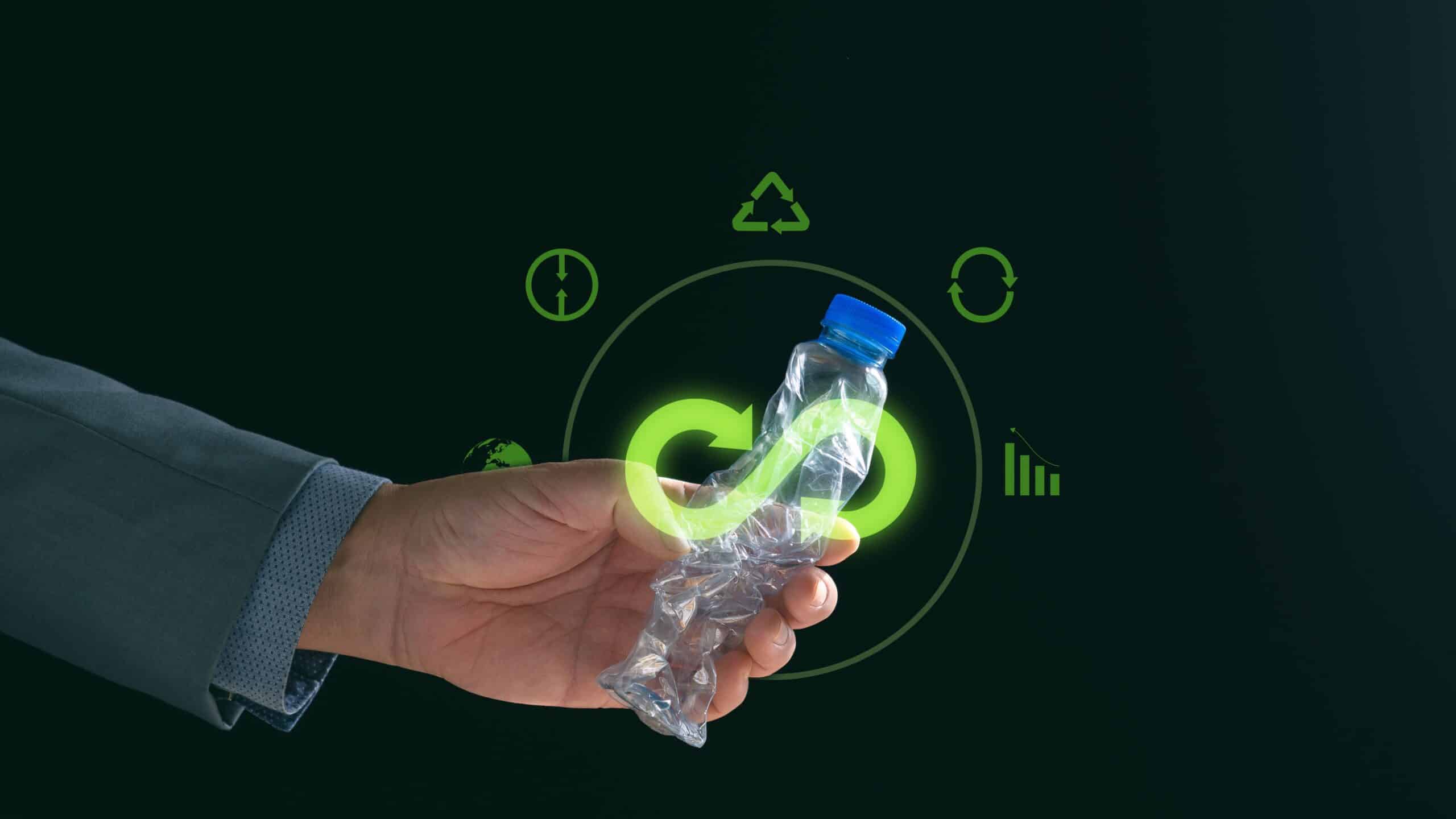 Mano sujetando una botella de plástico aplastada que tiene encima el símbolo del infinito y un círculo alrededor con iconos que simulan economía circular.