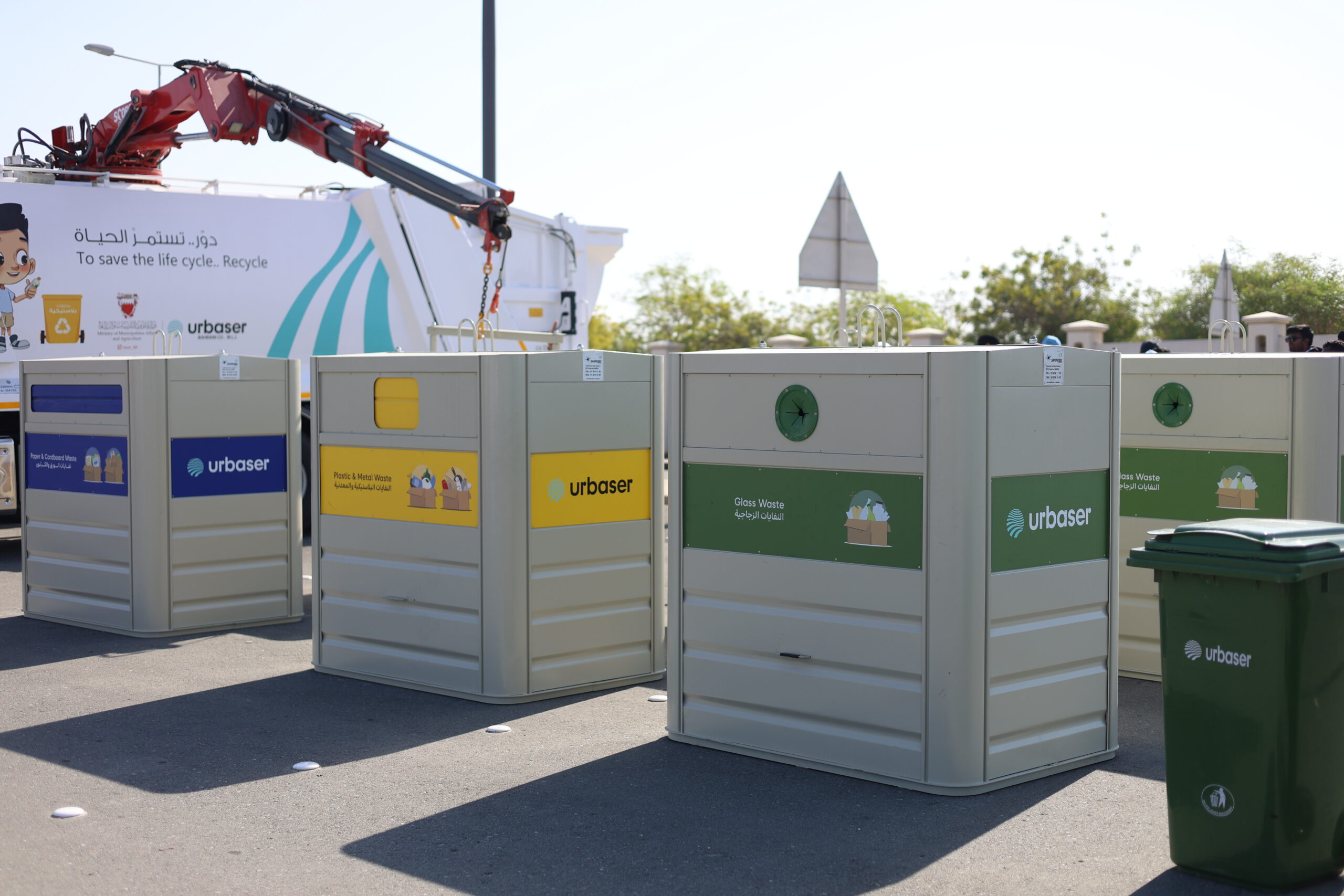 Contenedores de reciclaje de Urbaser para papel, envases y vidrio en vía pública, junto a un camión de recogida.